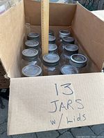 Box containing 13 large CROWN preserve jars with glass lids and metal rings, showing ruler for scale.