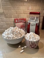 Electric air popcorn maker setup with popcorn and boxes, popcorn on countertop and in cups.