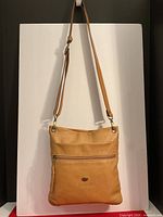 Front view of the tan leather crossbody bag with visible front zipper pocket and strap.