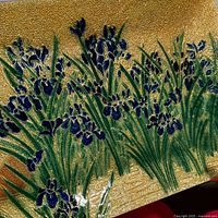 Close-up of cloisonné irises and leaves on textured gold background showing enamel details.