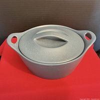 Front view of gray Corningware Creations covered stoneware dish with lid, placed on red surface.