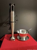 Full view of immersion blender, stainless steel bowl, and spoon on red cloth backdrop