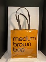Front view of the brown PVC tote bag with 'medium brown bag' text and grey handles visible.