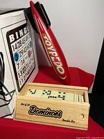 Photo showing the Bingo cage with cards, the Toypedo standing upright on a stand, and the wooden domino box with dominoes inside.