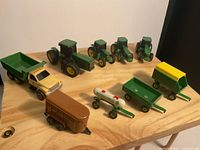 Front view of all John Deere collectible toys including tractors, truck, and various trailers arranged on wood surface.