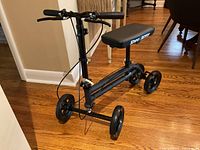 Side view of black Knee Rover scooter, showing padded seat, adjustable handlebar, four wheels, and frame structure.