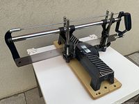 Side angle view of Mastercraft manual mitre saw on wooden base showing the metal frame, blade, handle, and adjustable clamps.