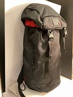 Side view of the black New Era rucksack backpack with cliple closures and visible interior red lining.