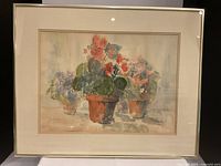 Original watercolour painting titled "The Red Pot" by Jacy Kington framed under glass, showing red flowers in terracotta pots with a beige mat and silver-colored frame.