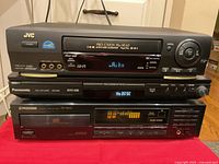 Three media players stacked: JVC VHS on top, Panasonic DVD/CD player in middle, Pioneer CD player at bottom.