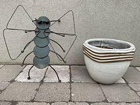 Photo showing the metal bug sculpture with wire legs and circular segmented body standing next to the white and brown decorative clay planter pot.