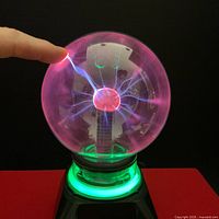 Plasma ball turned on showing electric arcs triggered by finger touch, with green illuminated base.