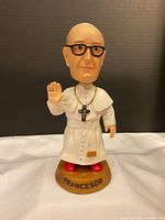 Front view of Pope Francis bobblehead figurine with white robe, glasses, and 'FRANCESCO' base