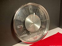 Front angled view of round quartz wall clock with silver and clear plastic construction.