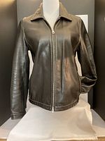 Front view of the black leather jacket on a mannequin, showing a full zip and collar.