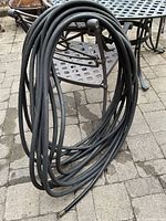 Coiled black rubber hose hanging on a metal chair outdoors on a paved patio.