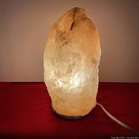 Front angled view of Himalayan salt lamp illuminated showing warm amber glow and natural crystal texture.