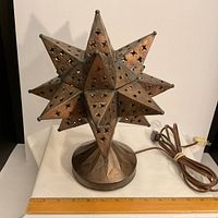 Front view of copper/bronze star-shape lamp sitting on table with ruler for scale