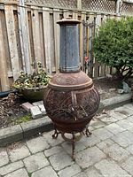 Full view of the chiminea standing on patio, showing spherical mesh body and chimney top.