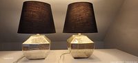 Front view of two matching lamps showing textured reflective mercury glass bases with square edges and black shades.