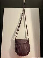 Front view of soft plum leather purse with long strap hanging against white background.