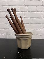 Six wooden rolling pins standing inside a ceramic container against a white brick wall background.