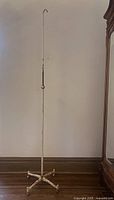 Full height view of tall white antique hospital IV stand showing adjustable height and hook at top.