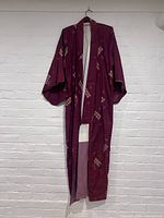 Front full view of burgundy antique kimono hung on hanger against white wall showing entire garment and interior lining.