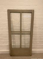 Front view of the antique painted wooden storm window with four glass panels and mullions against a brick wall.