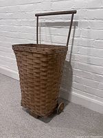 Front angled view showing the woven wicker pattern, wooden handle, and wheels