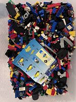 Pile of assorted LEGO bricks with instruction sheet on top, showing various colored bricks and pieces.