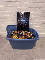 Large blue plastic bin filled with assorted K'nex pieces with original instruction manual standing inside the bin.