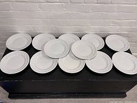 Top down view of 12 white antique ironstone dinner plates laid out flat showing scalloped and embossed edge detail.