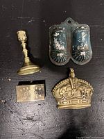 Top-down view showing all four items: brass candlestick, Victorian tin match holder with blue paint, brass matchbox holder with engraved Sverige and flags, and gold painted plaster crown.