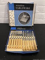 Full set of cutlery inside the original blue and white striped box labeled 'stainless TABLEWARE'.