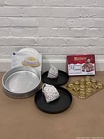 Photo showing two metal 9-inch tart pans with removable bottoms, two bags of white pie weights, two 10-inch Wilton round cake pans, Nordic Ware mini loaf/treat pan, 3D gingerbread cookie cutter set box, and cardboard cake circles in the background.