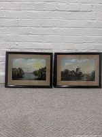 Both framed paintings side by side against a white brick wall and carpeted floor.