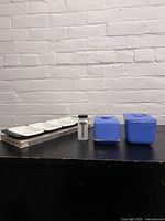 Full view of lot on black table showing white serving tray with 5 dishes, antique clove container, and 2 blue Westinghouse containers