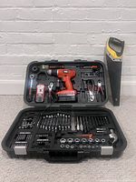 Black & Decker cordless drill tool set open displaying drill, various drill bits, sockets, screwdriver bits, hand tools, and charger inside black carrying case.