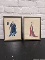 Two framed costume sketches from Stratford Festival 1977 displayed side by side against a white brick wall.
