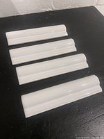 Four white curved coping tiles arranged on a black surface showing the glossy finish and curved top edge.