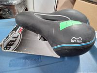 Black Bell Soft-Tech padded bike seat still attached to its original cardboard backing, showing the seat's ergonomic cutout and brand markings.