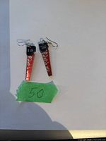 Photo of the pair of earrings shaped like miniature hand saws, red blades with silver detail and black handles with hooks.