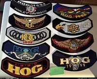 Nine Harley Davidson H.O.G. owner patches laid flat on a wooden surface. Each patch has year and Harley Davidson logo or related design from 1991 to 1999.