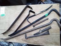 Six crow bars of varying sizes and shapes arranged on a wooden surface, showing usage wear and rust patches.