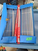 Blue plastic case open showing multiple metal knitting needles secured with elastic bands, including sets from Clover brand in red packaging.