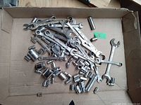 Box of assorted metal hand tools including combination wrenches and multiple sockets.