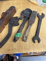 Photo of five vintage hand tools on wooden surface: wooden hand plane, two adjustable wrenches, wooden mallet, and open-end wrench.