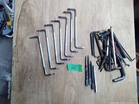 Photo shows a collection of hand tools arranged on a wooden surface. Left group contains 9 L-shaped Allen keys. Middle items are 2 metal punches. Right group is a mixed pile of offset screwdrivers and various Allen keys.