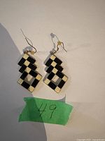 Pair of black and white checkerboard dangle earrings laid on white surface with green paper labeled '49'.